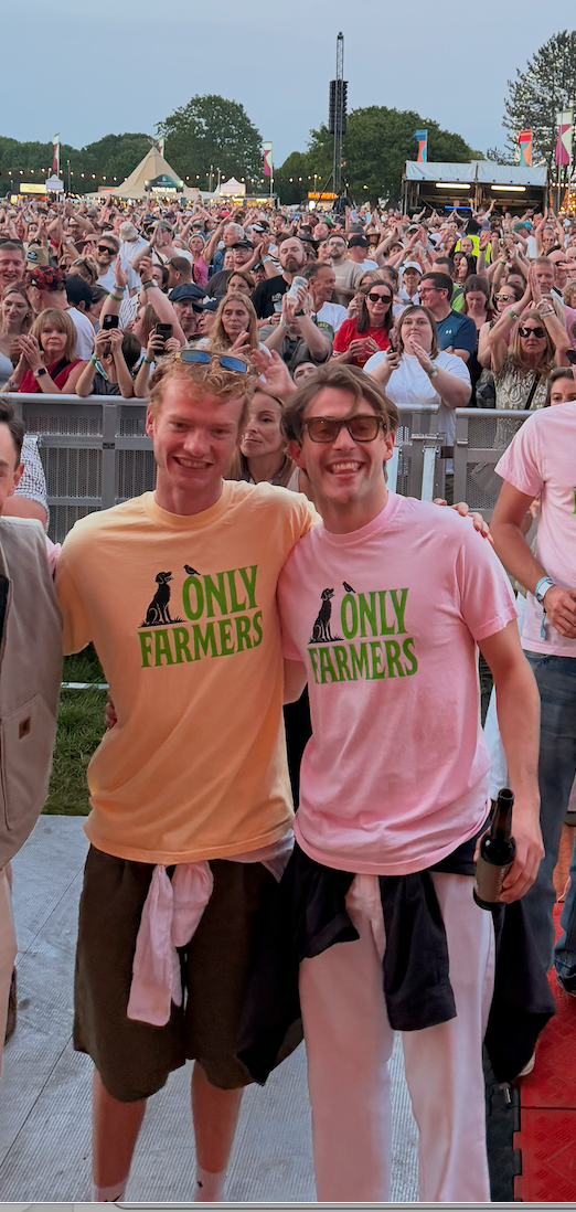 Two men wearing 'Only Farmers' t-shirts standing in front of a crowd at an outdoor event.